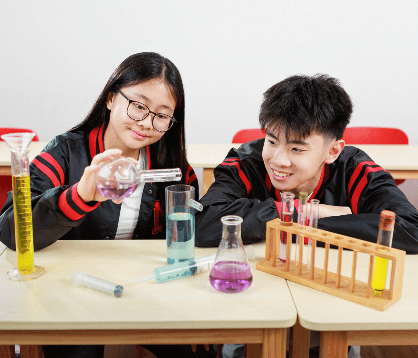 Two secondary students in Mavis jackets conducting a chemistry experiment with test tubes and coloured solutions
