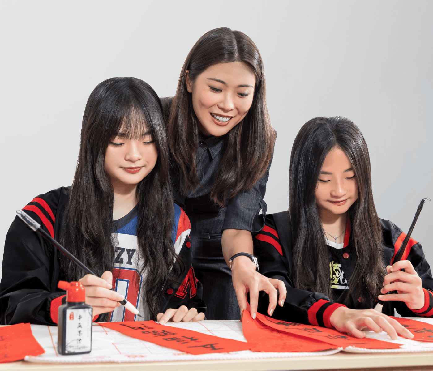 A Mavis tutor guiding two students practising Chinese calligraphy with brush and ink